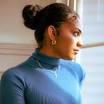 Portrait of a woman in a blue turtleneck gazing out a window, exuding elegance.