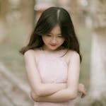 Portrait of a young woman with long hair in a pink lace dress, outdoors in a serene setting.